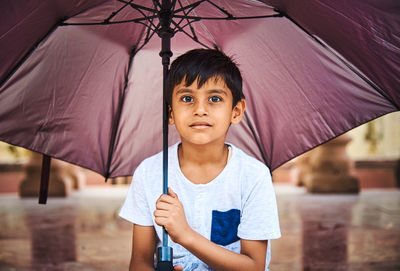 Portrait of cute boy holding umbrella standing outdoors