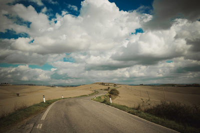 Empty road amidst field against sky