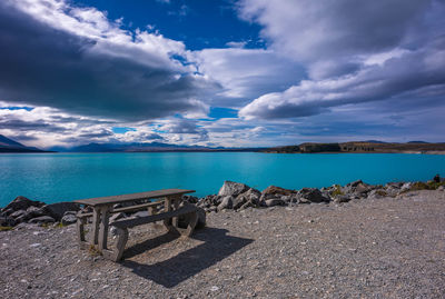 Empty bench and table by lake pukaki against cloudy sky