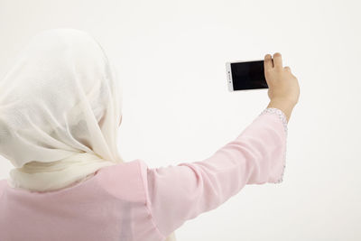 Midsection of man photographing with mobile phone against white background