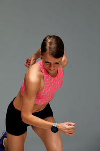 Side view of young woman exercising against gray background