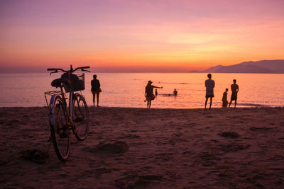 Bicycle against silhouette people standing at beach during sunset