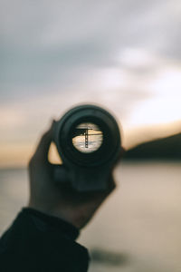 Close-up of hand holding monocular against sky