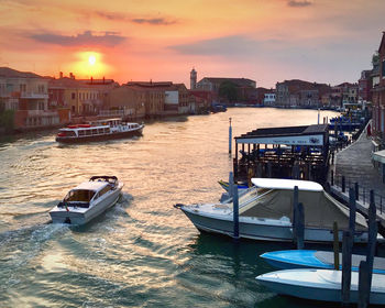 Boats moored in canal by buildings against sky during sunset