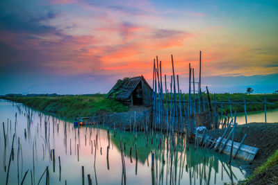 Scenic view of lake by house against sky during sunset