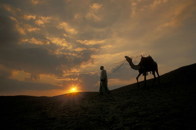 Rear view of man standing on field against sky during sunset