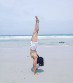 Full length of young woman doing handstand at beach against clear sky