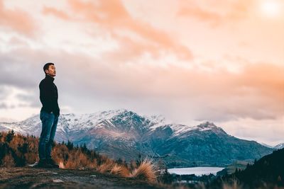 Full length of man standing on mountain against cloudy sky during sunset