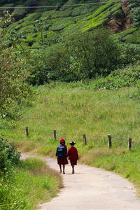 Rear view full length of girls walking by grassy field on road