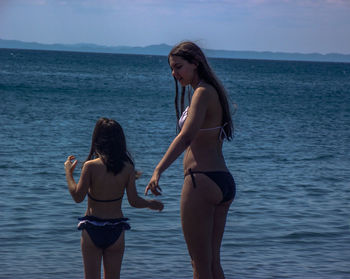 Rear view of woman and daughter standing in sea