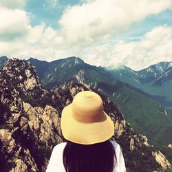 Rear view of woman wearing hat looking at mountains against sky