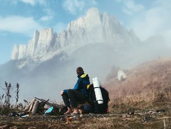 Man sitting on field near mountains during foggy weather