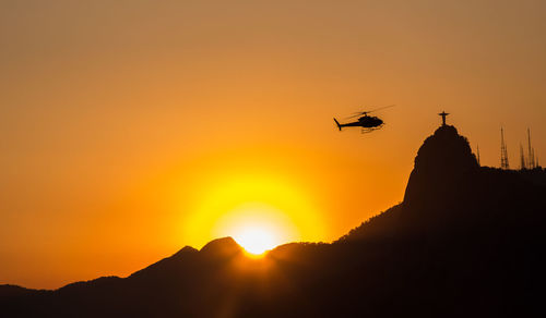 Low angle view of silhouette airplane flying against orange sky