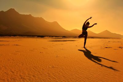 Silhouette woman with arms raised on beach against sky during sunset