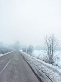 Road by snow covered landscape against sky