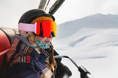 Portrait of a professionally dressed female skier in profile sitting in an open cabin of a ski lift