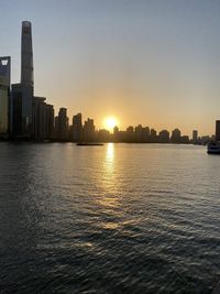 Sea by buildings against sky during sunset