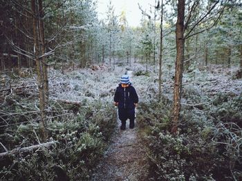 Rear view of man standing amidst trees in forest