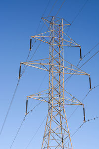 Low angle view of electricity pylon against clear blue sky