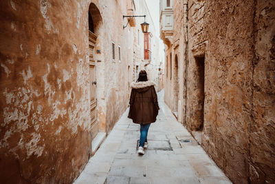 Rear view of woman walking on alley amidst buildings