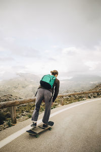 Male backpacker skateboarding on road against sky