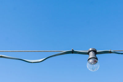 Light bulb hanging on wire against clear blue sky