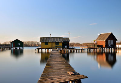 Pier over lake by houses against blue sky