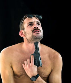 Shirtless man attempting suicide with gun against black background