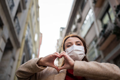 Low angle portrait of woman wearing mask standing against sky