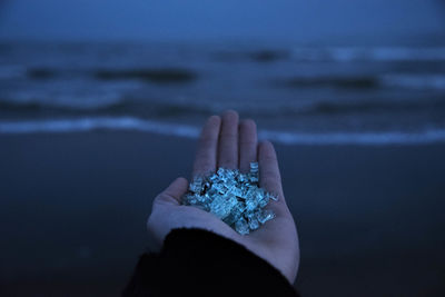 Cropped hand holding crystals at beach during dusk