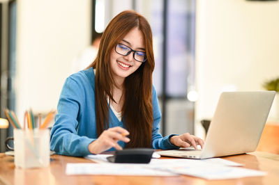 A young asian businesswoman working with laptop and calculator, girl with glasses working happily.