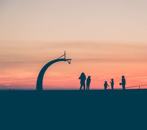 Silhouette children playing basketball against sky during sunset