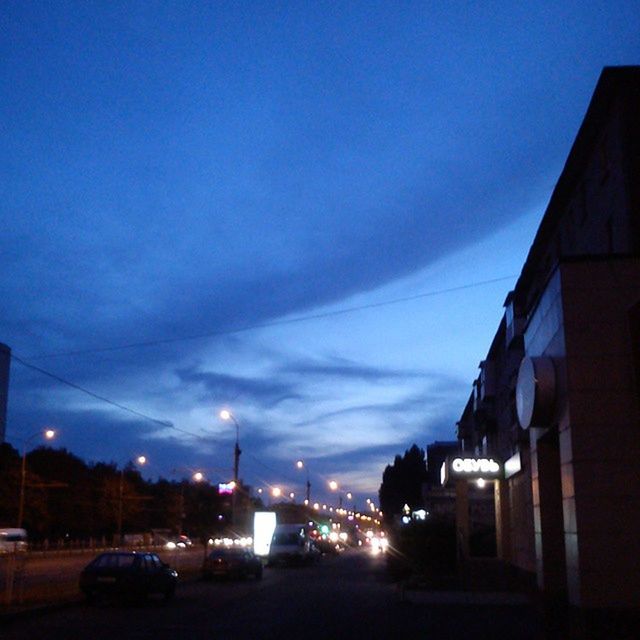 building exterior, architecture, built structure, sky, transportation, road, car, street, city, dusk, cloud - sky, street light, land vehicle, the way forward, illuminated, blue, cloud, silhouette, outdoors, sunset