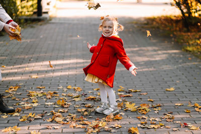 Full length of girl with autumn leaves on footpath
