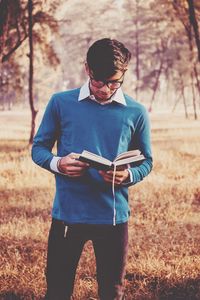 Young man reading book on field