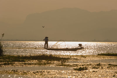 Silhouette man on sea against sky during sunset