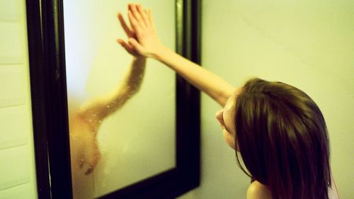 The beautiful woman with wet hair looks in a mirror in a bathroom