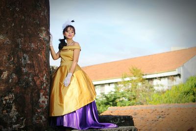 Young woman wearing evening gown while standing by weathered wall