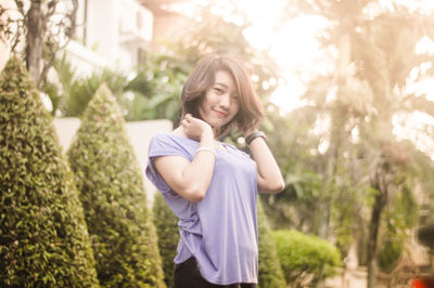 Portrait of beautiful woman with hands in hair standing against trees