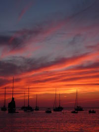 Silhouette sailboats sailing on sea against dramatic sky during sunset