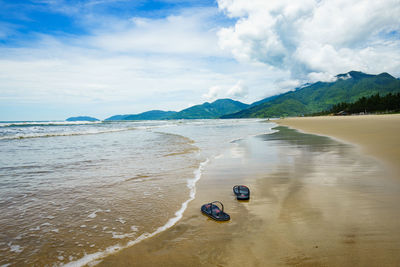 Flip-flops at beach against cloudy sky