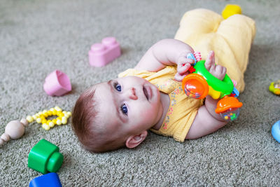 Cute little baby girl lying on a floor and playing with colorful plastic and wooden toys. 