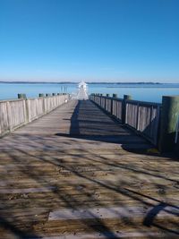 Wooden pier on beach against clear blue sky