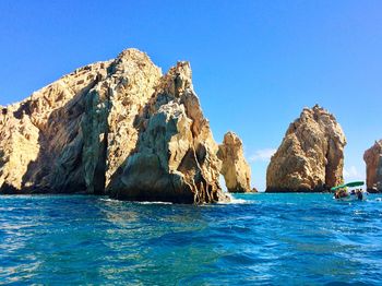 Rock formations in sea against clear blue sky
