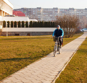 Full length of man riding bicycle on footpath at park in city