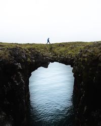 Man standing on rock by sea against clear sky