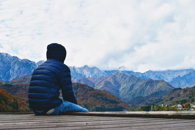 Rear view of man looking at mountains against sky during winter