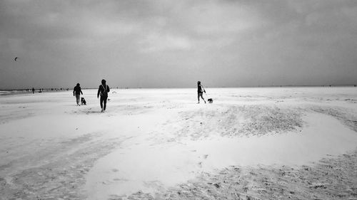 People walking on snow covered beach against cloudy sky