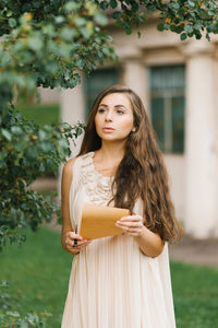 A romantic young woman in a summer dress holds a vintage letter in her hands