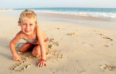 Portrait of smiling girl kneeling at beach against sky